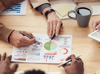multiple hands pointing to financial graphs on the table